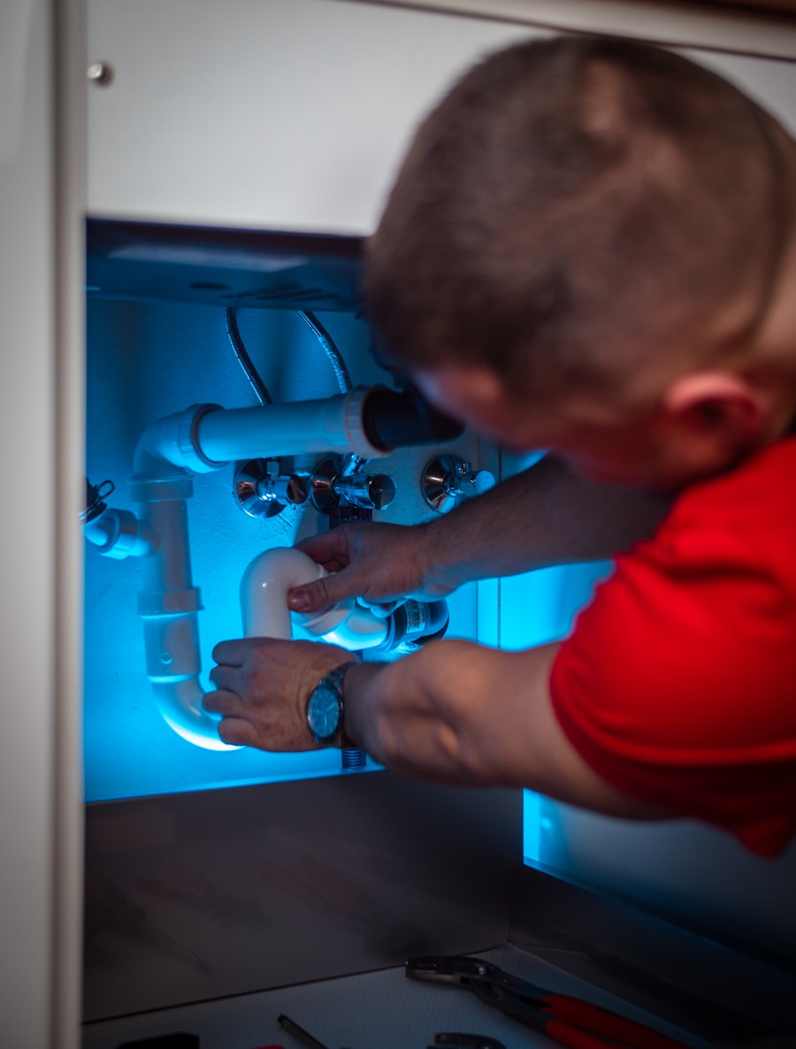 A plumber working on under-sink plumbing in a kitchen cabinet