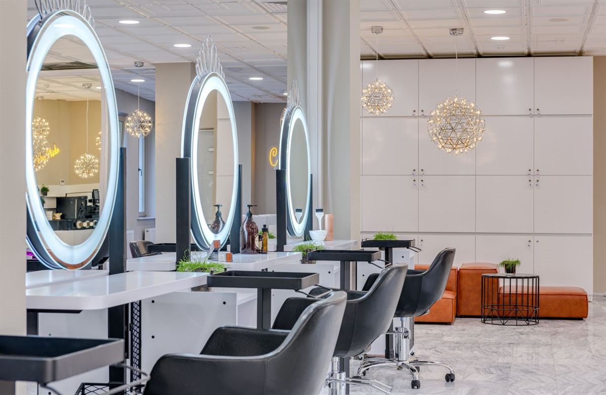 Salon styling stations with lit round mirrors and black leather chairs