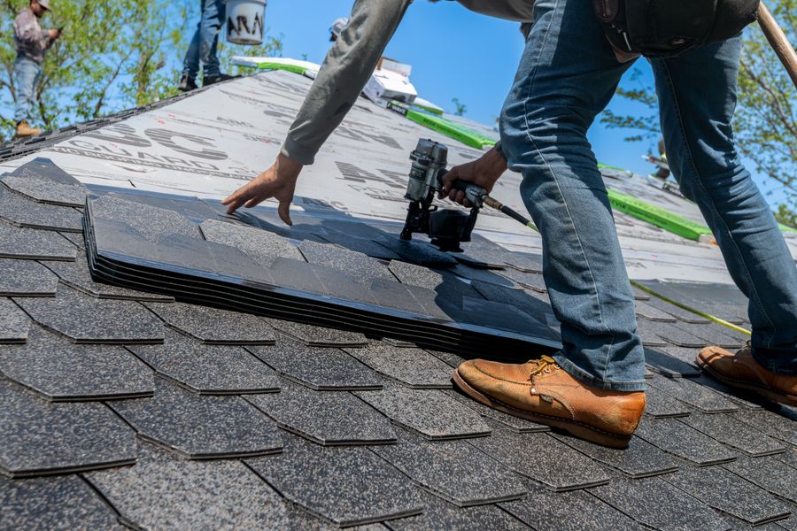 A crew member nailing architectural shingles on a steep roof