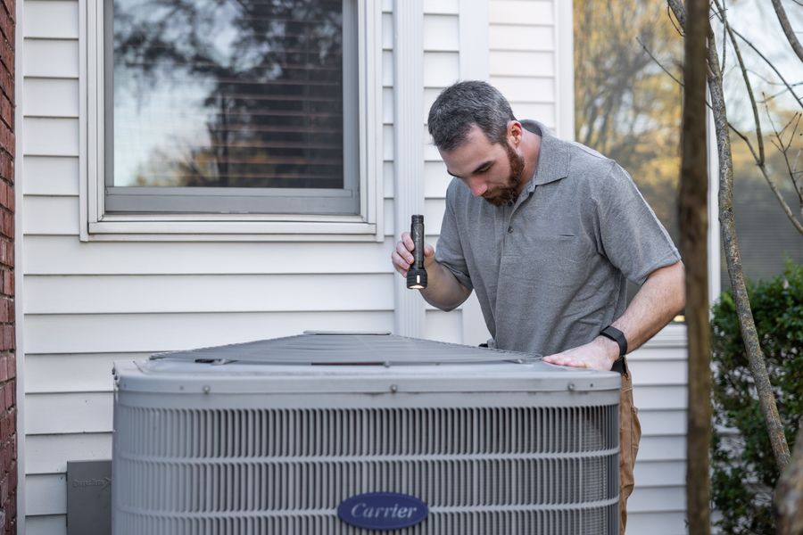 A Wasatch Air technician inspecting an outdoor A/C condenser with a flashlight
