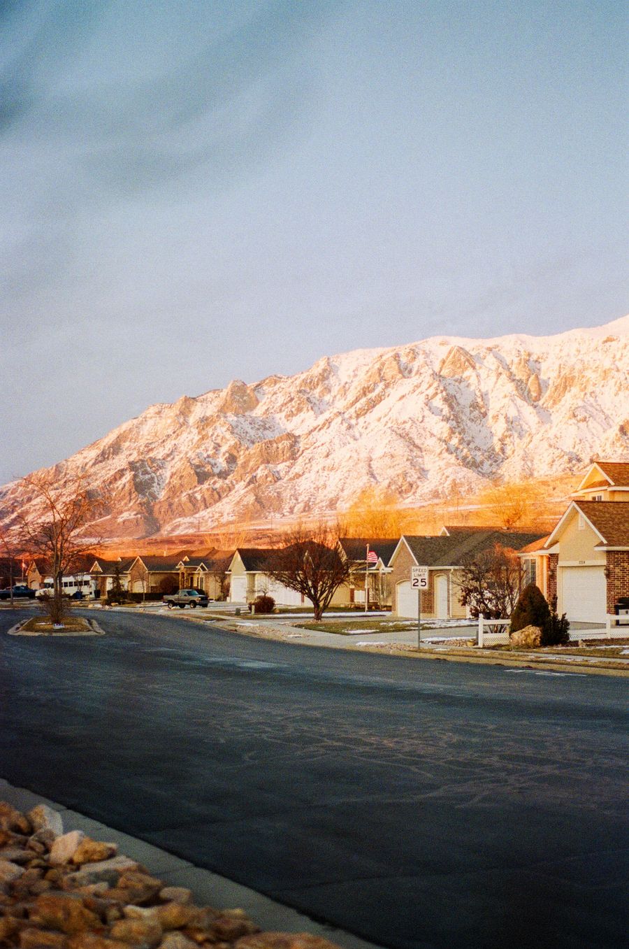 A Weber County neighborhood street at dusk with the snowy Wasatch range glowing behind the homes